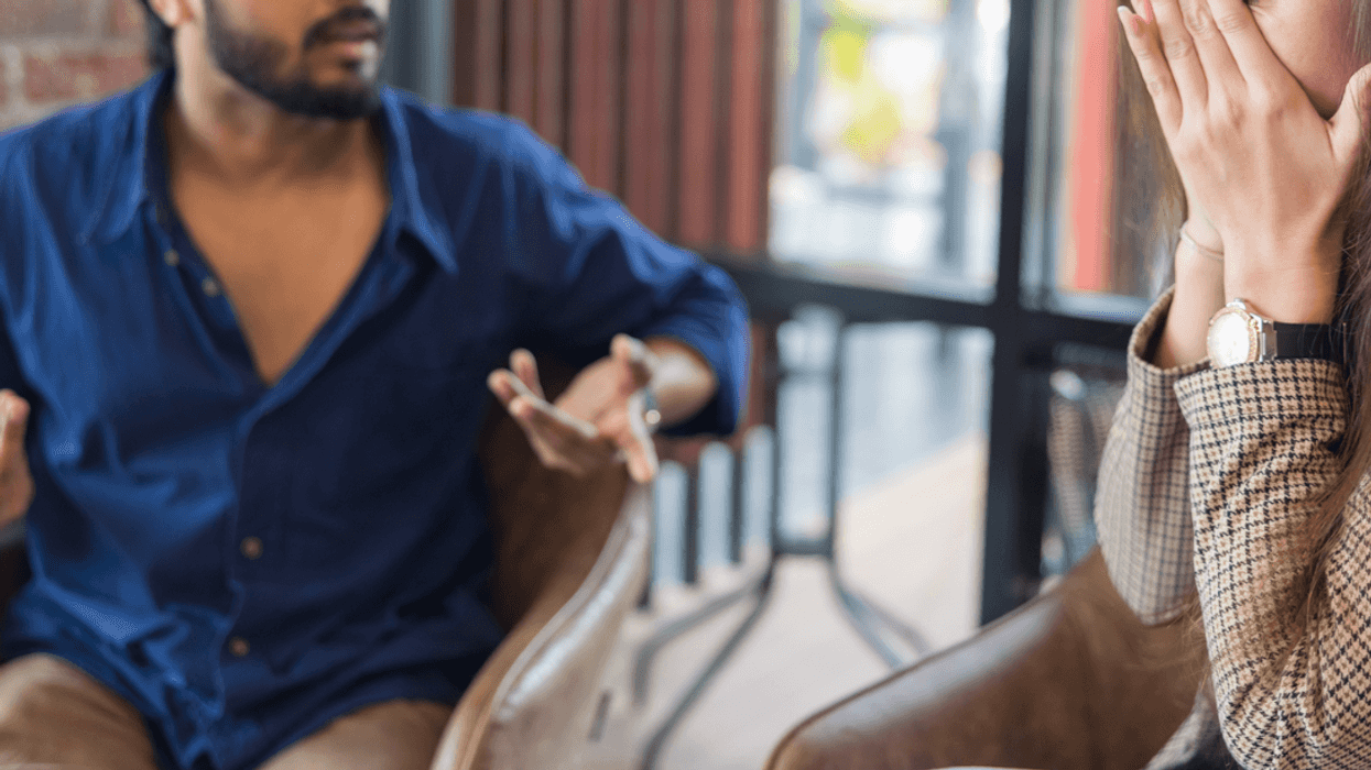A woman covering her fave sitting next to a man making emmphatic gestures.