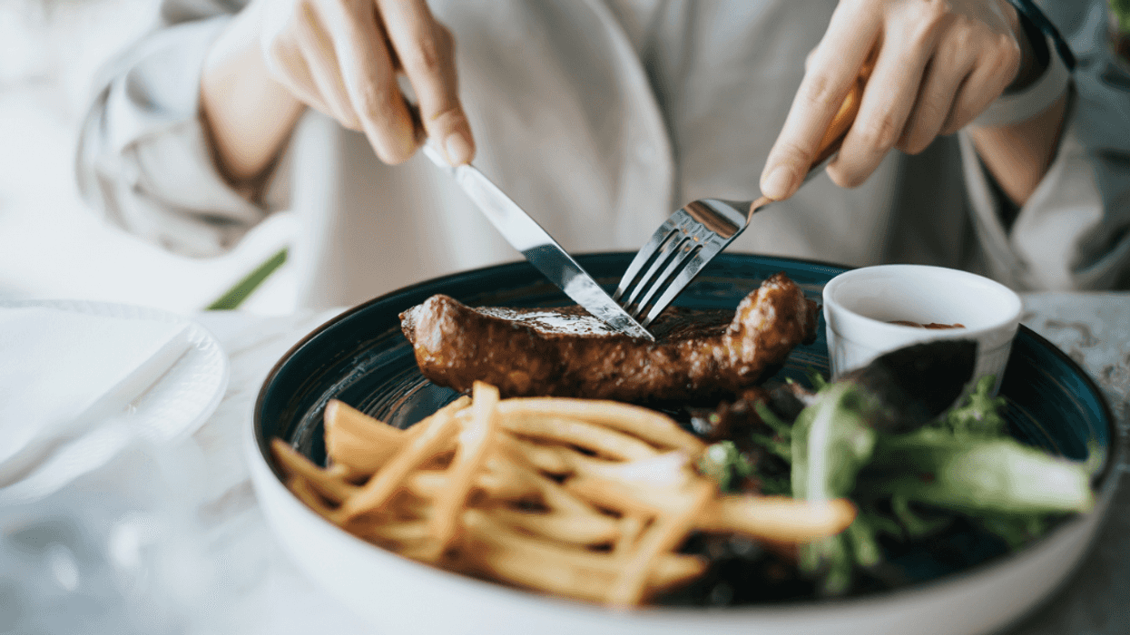 A woman cutting into a steak with french fries and salad greens sharing the plate.