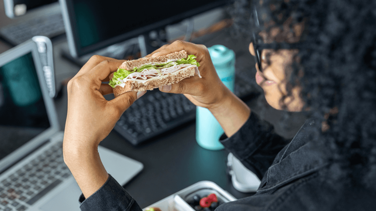 A woman eating a sandwich while sitting at her computer.