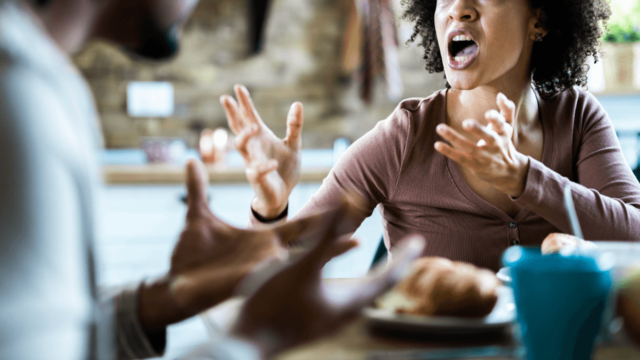 A woman emphatically gesturing at a man across a table from her.