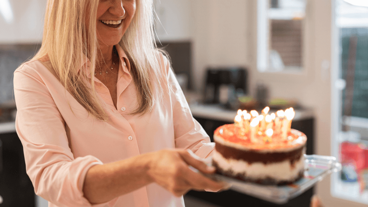 A woman holding a birthday cake with lit candles in it.