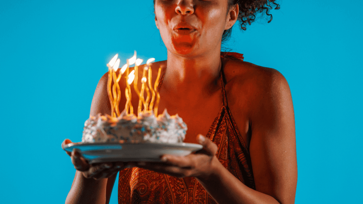 A woman holding a cake with birthday candles in it, blowing them out.