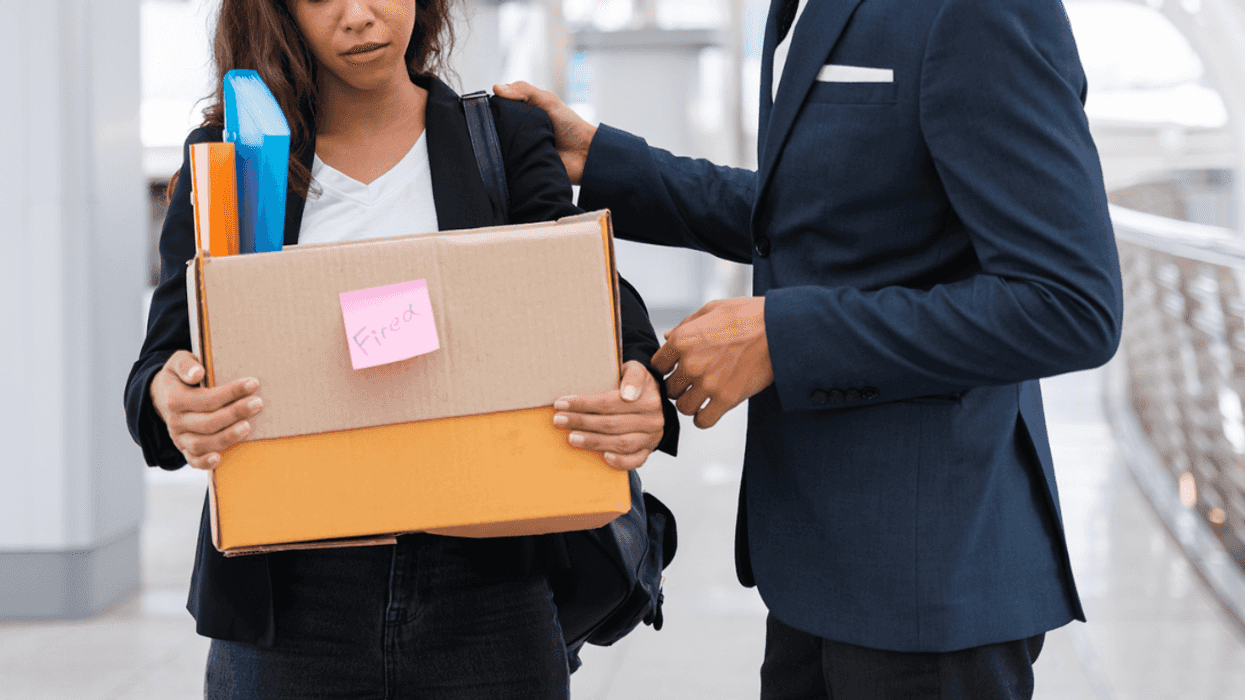 A woman holding a cardboard box full of items, with a man standing next to her resting his arm on her shoulder.