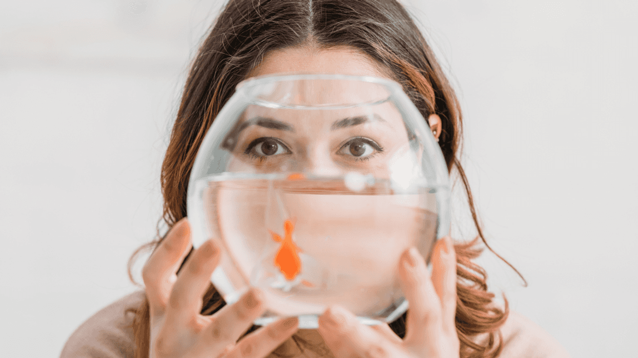 A woman holding a fishbowl in front of her face with a swimming goldfish in it.