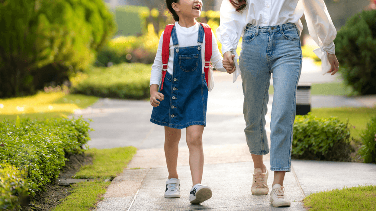 A woman holding a little girl's hand walking down the sidewalk.