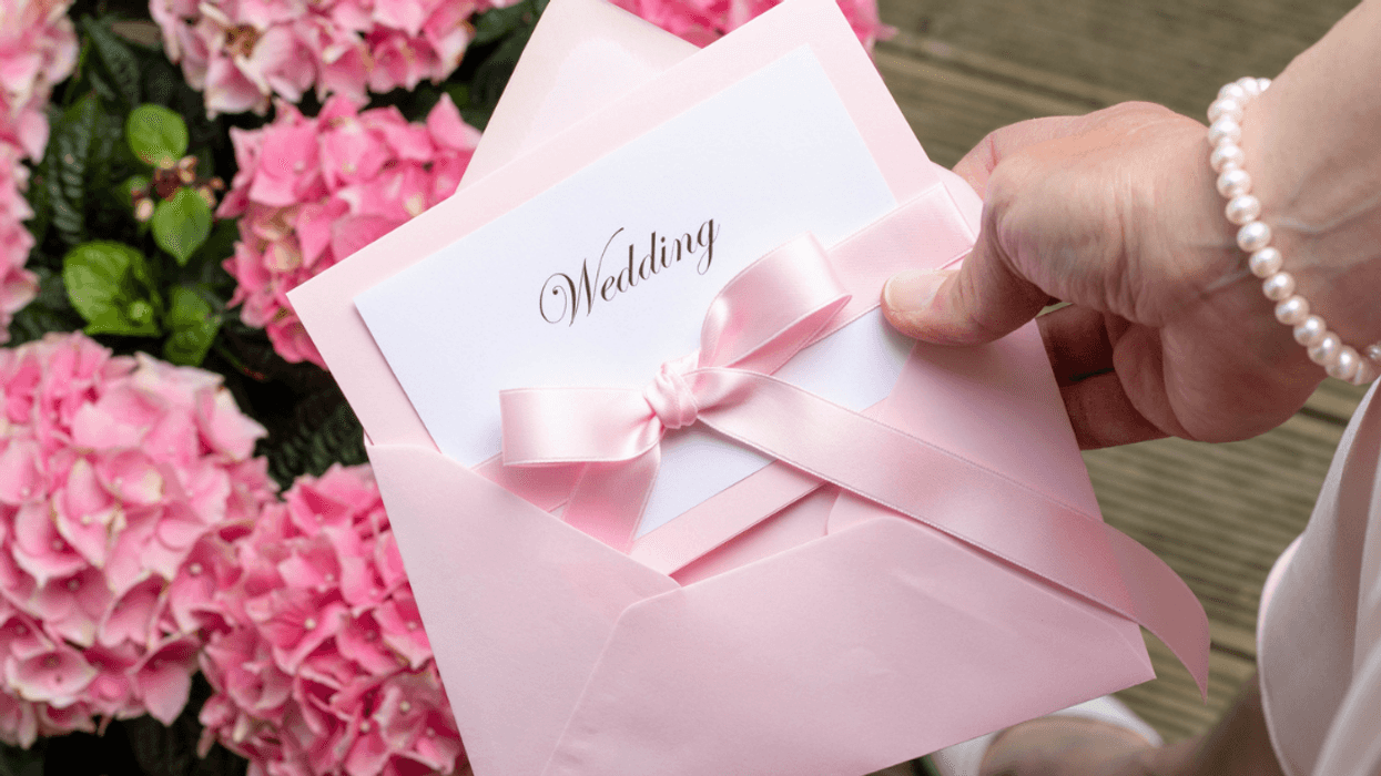 A woman holding a pink envelope with a card inside it with the word "wedding" written on it.