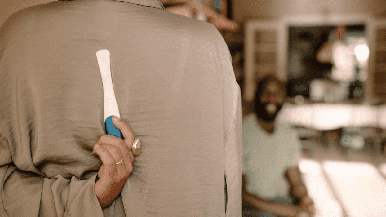 A woman holding a pregnancy test behind her back with a man facing her.