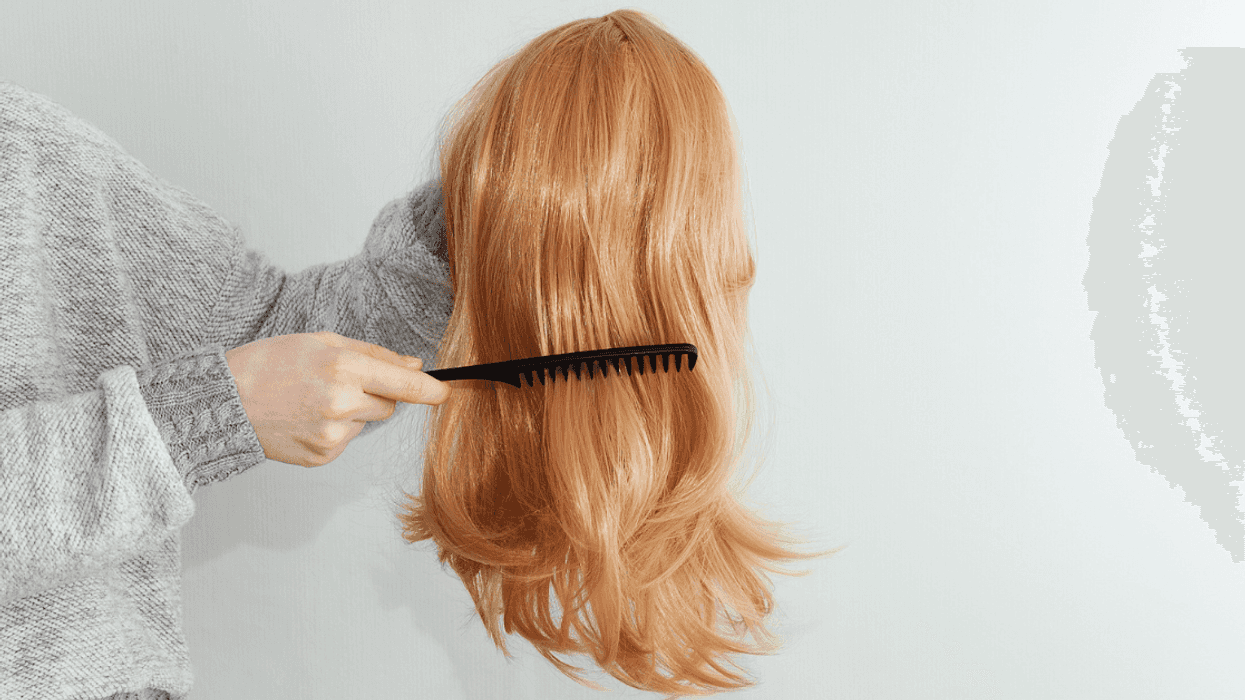 A woman holding a wig and running her comb through it.