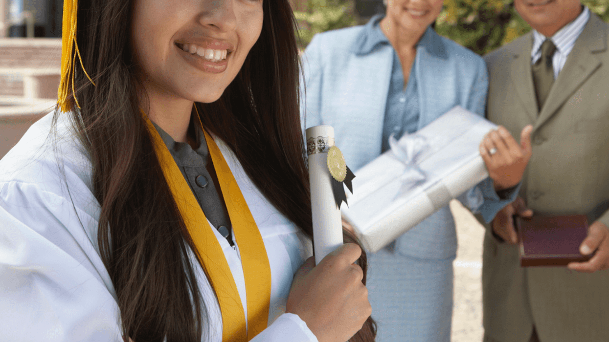 A woman in a graduation cap and gown and a couple standing in the background.