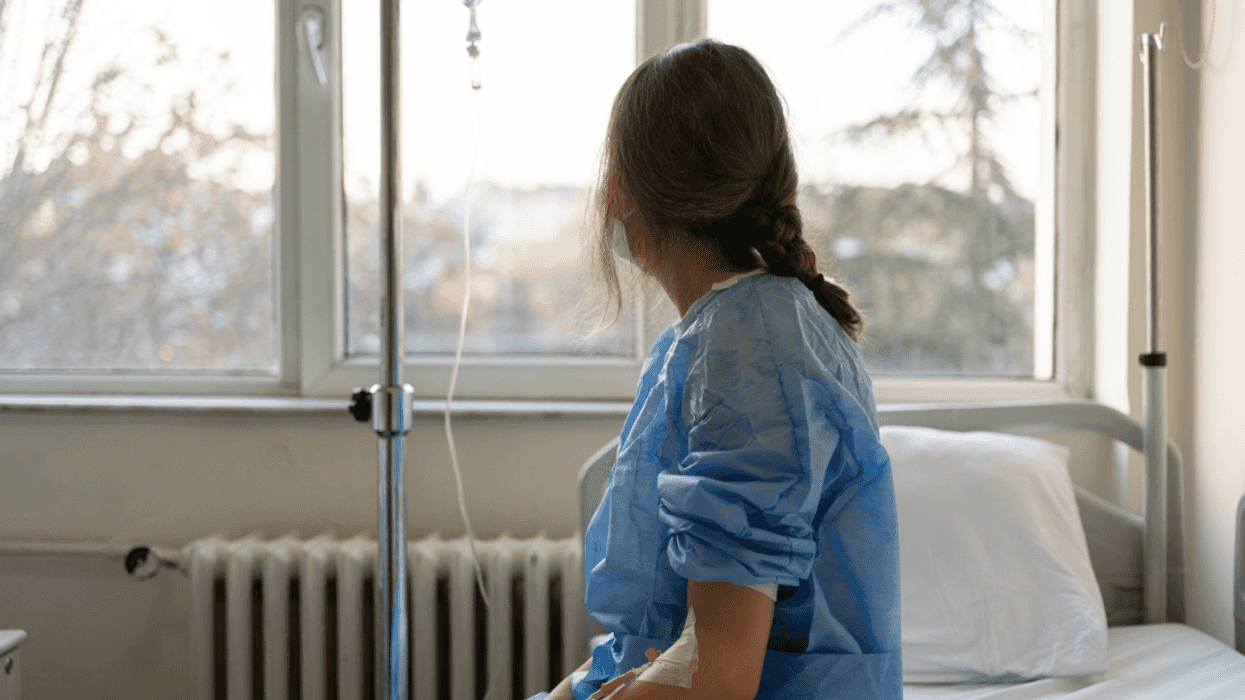 A woman in a hospital gowin sitting on a hospital bed looking out a window.