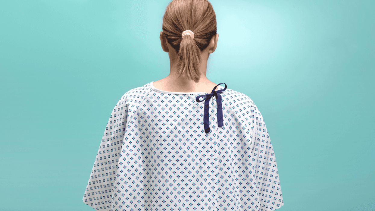 A woman in a hospital gown facing the back wall.