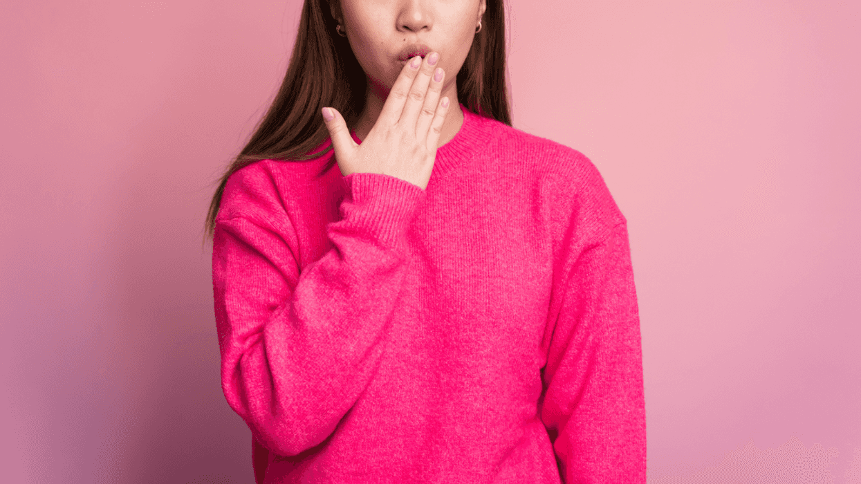 A woman in a pink sweater with her hand covering her mouth.