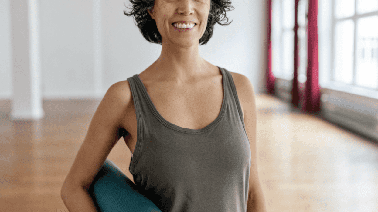 A woman in a tank top holding a yoga mat.