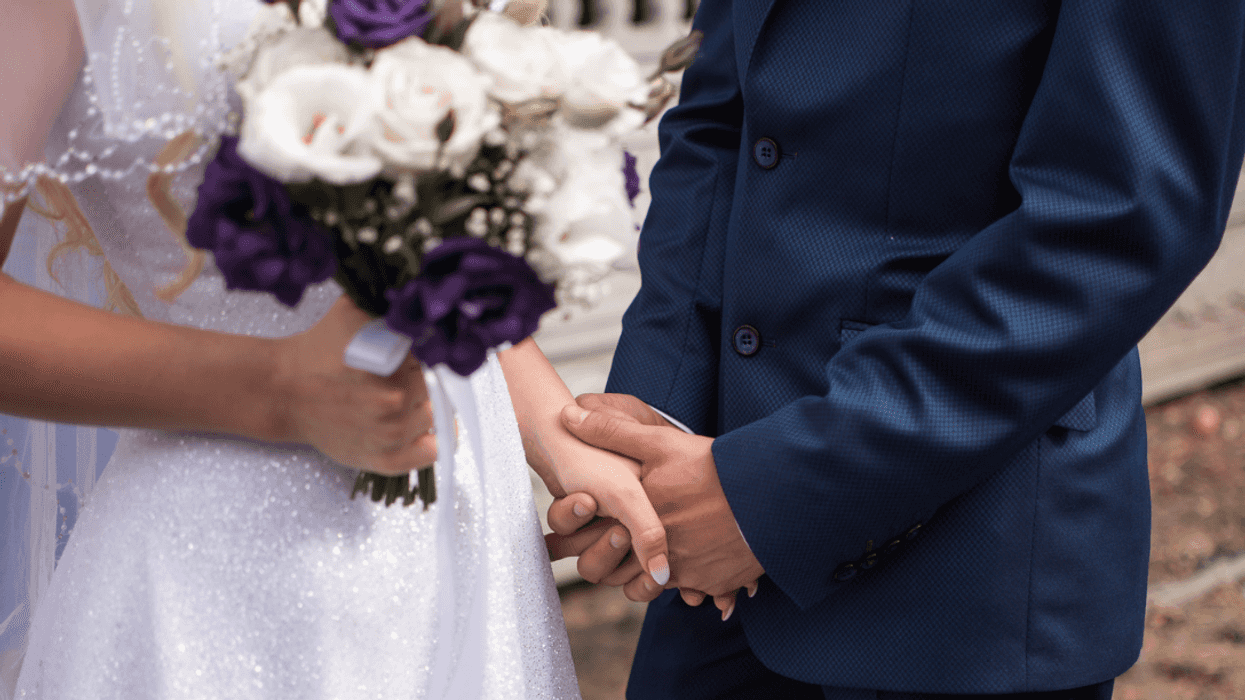 A woman in a wedding dress holding as bouquet holding a man's hand.
