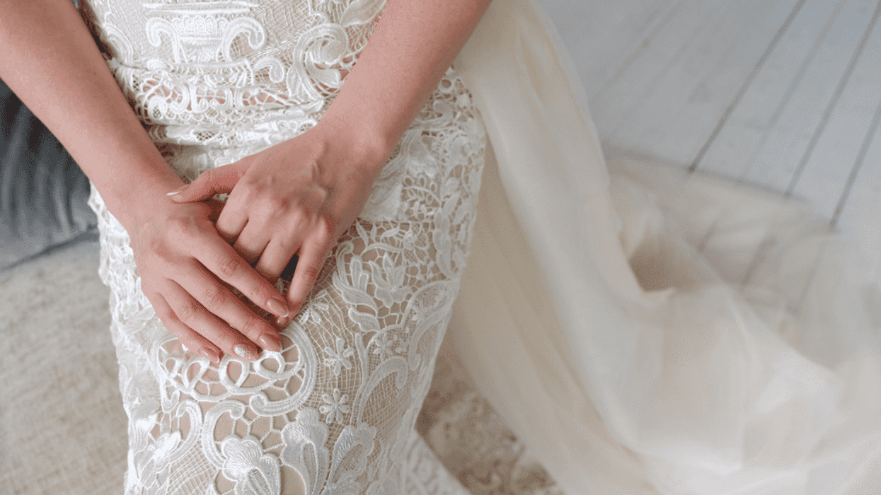 A woman in a wedding dress, sitting down with her hands in her lap.