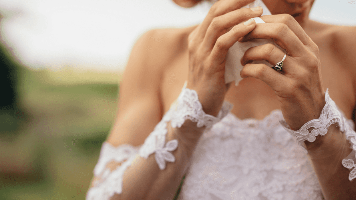 A woman in a wedding dress wiping tears from her eyes.