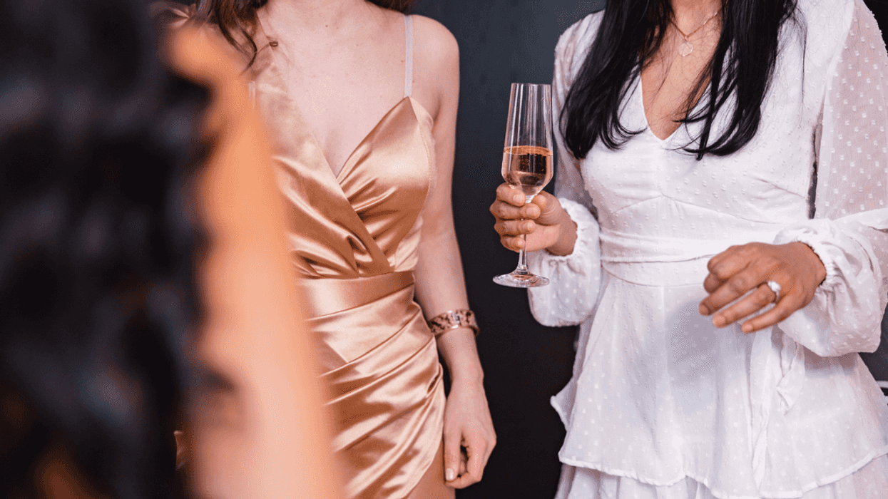 A woman in a white dress holding a glass of Champagne talking to two other women.
