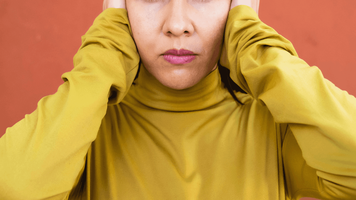 A woman in a yellow shirt covering her ears.