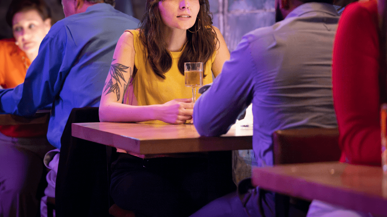 A woman in a yellow tank top with an arm tattoo sitting across a table form a man.