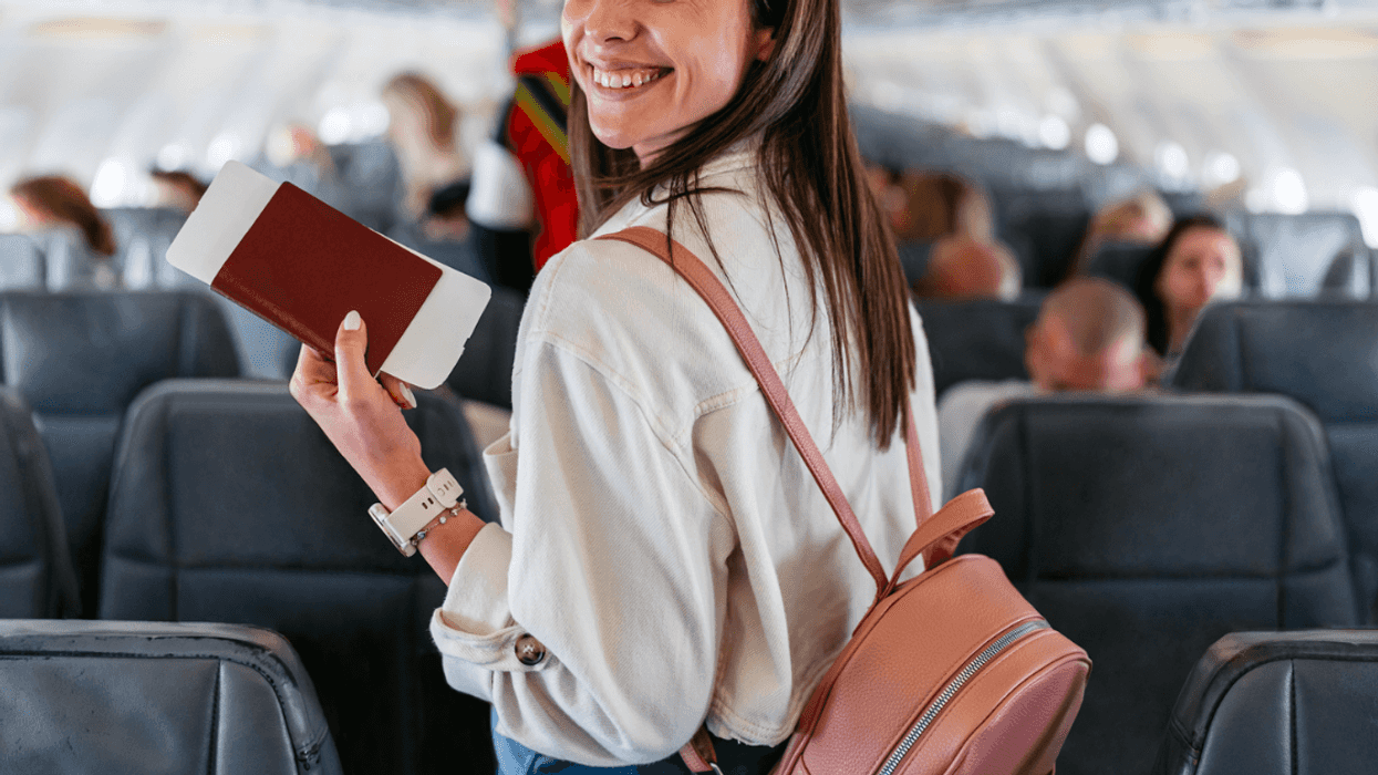 A woman in the aisle of an airplane holding her passport.