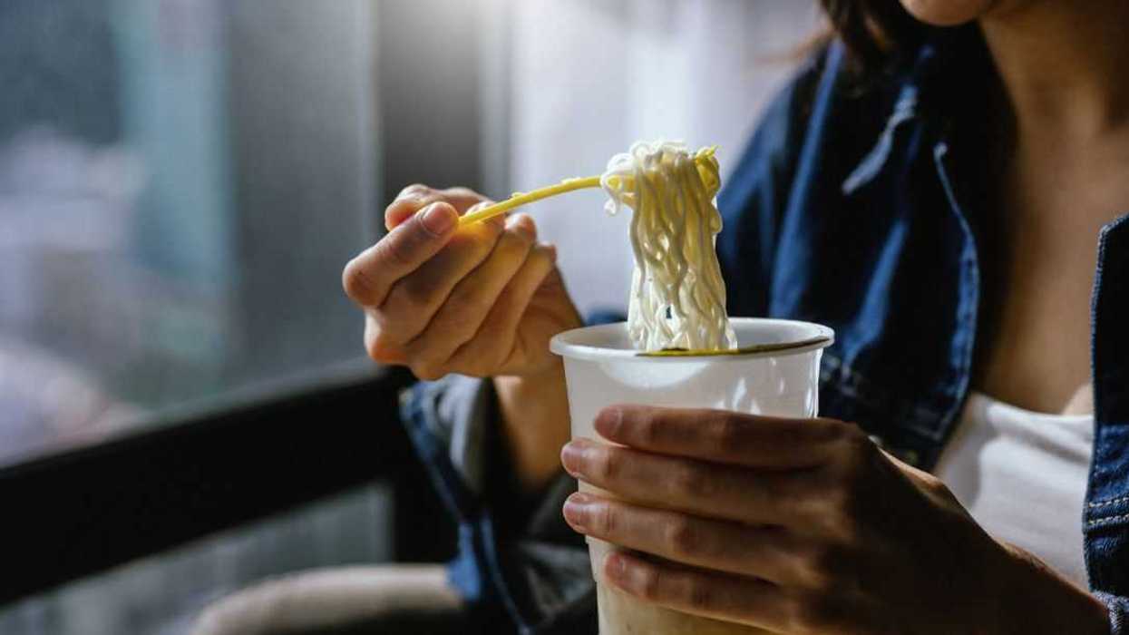 A woman is enjoying eating instant noodles in her living room at home.