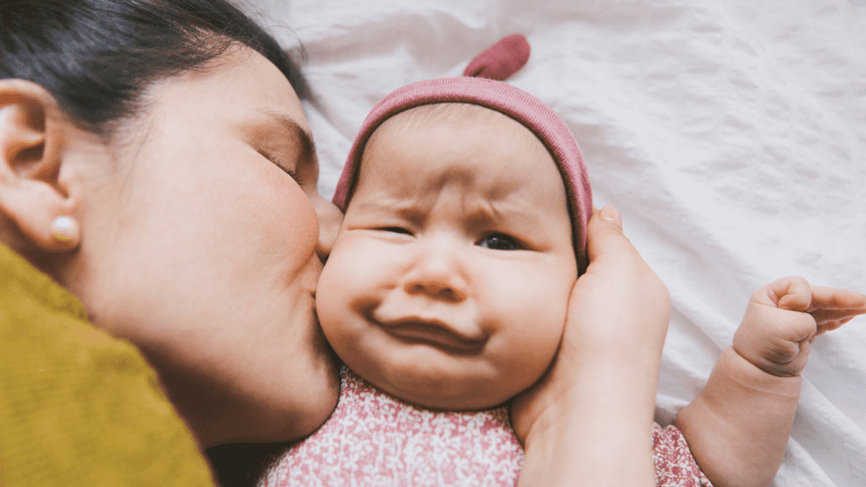 A woman kissing a baby with an awkward expression on her face.