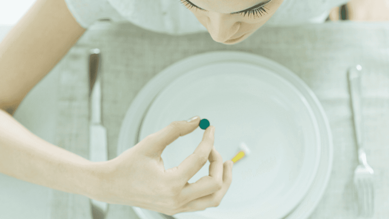 A woman leaning over an empty plate about to eat a small pea.