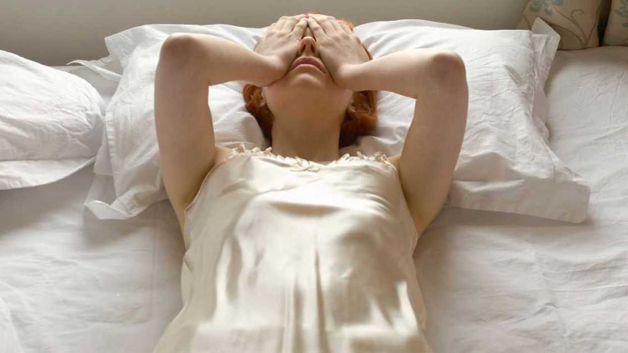 A woman lies back on a bed hands over her eyes