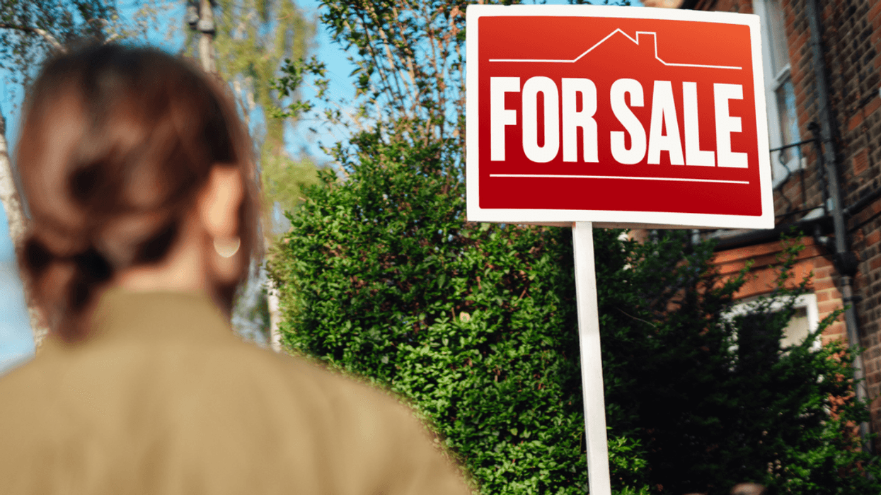 A woman looking at a "for sale" sign in front of her house.