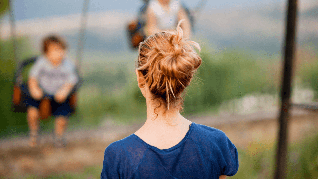 A woman looking at two children on swings.