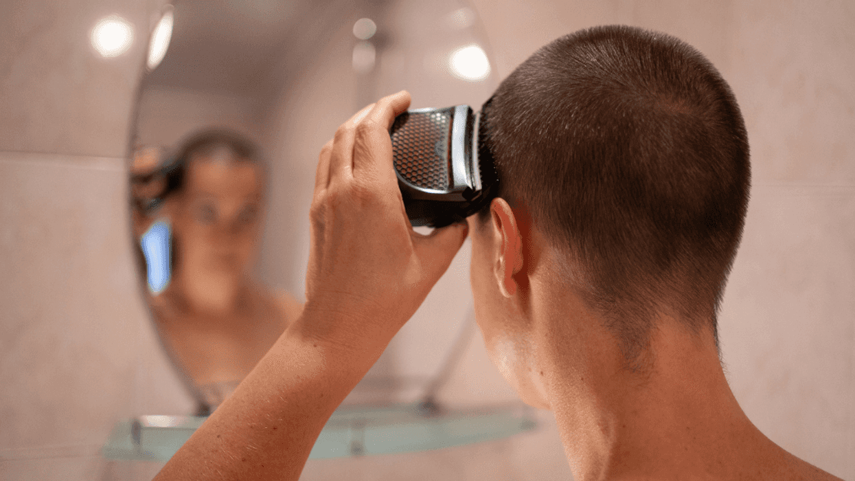 A woman looking into a mirror and shaving her head.