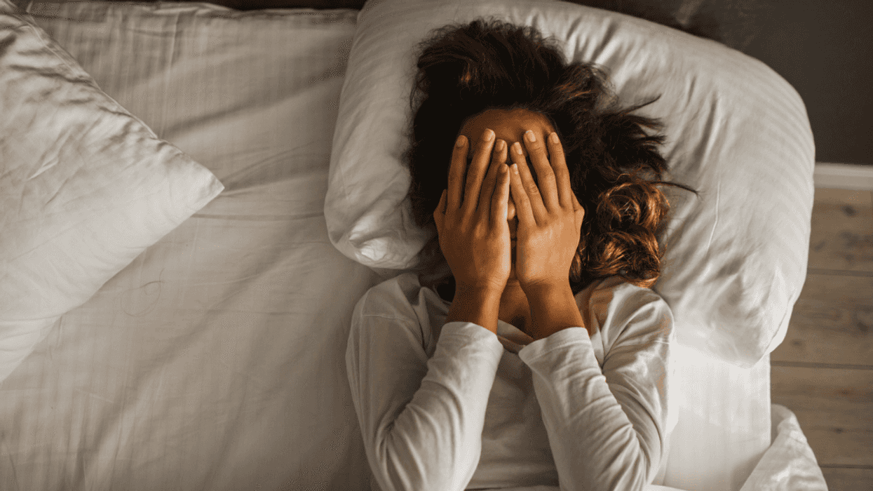 A woman. lying in bed covering her face.