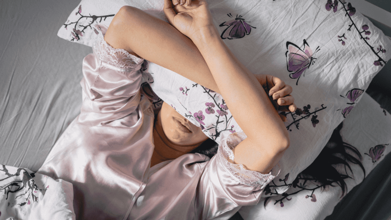 A woman lying in bed with a pillow covering her eyes.