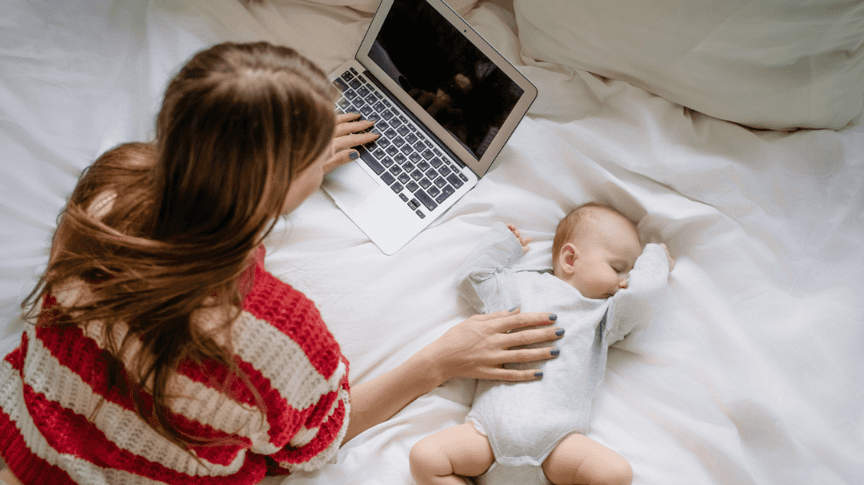 A woman lying on the bed in front of a laptop with a baby by her side.