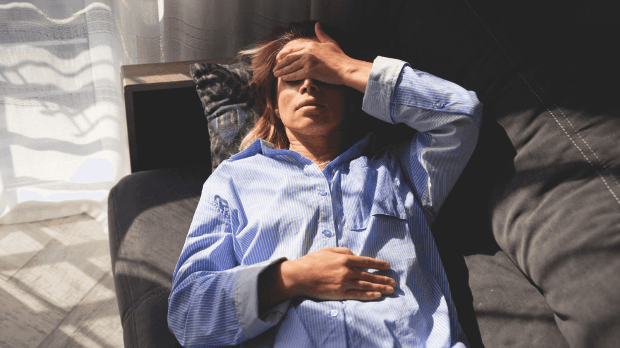 A woman lying on the sofa holding her hand over her eyes.