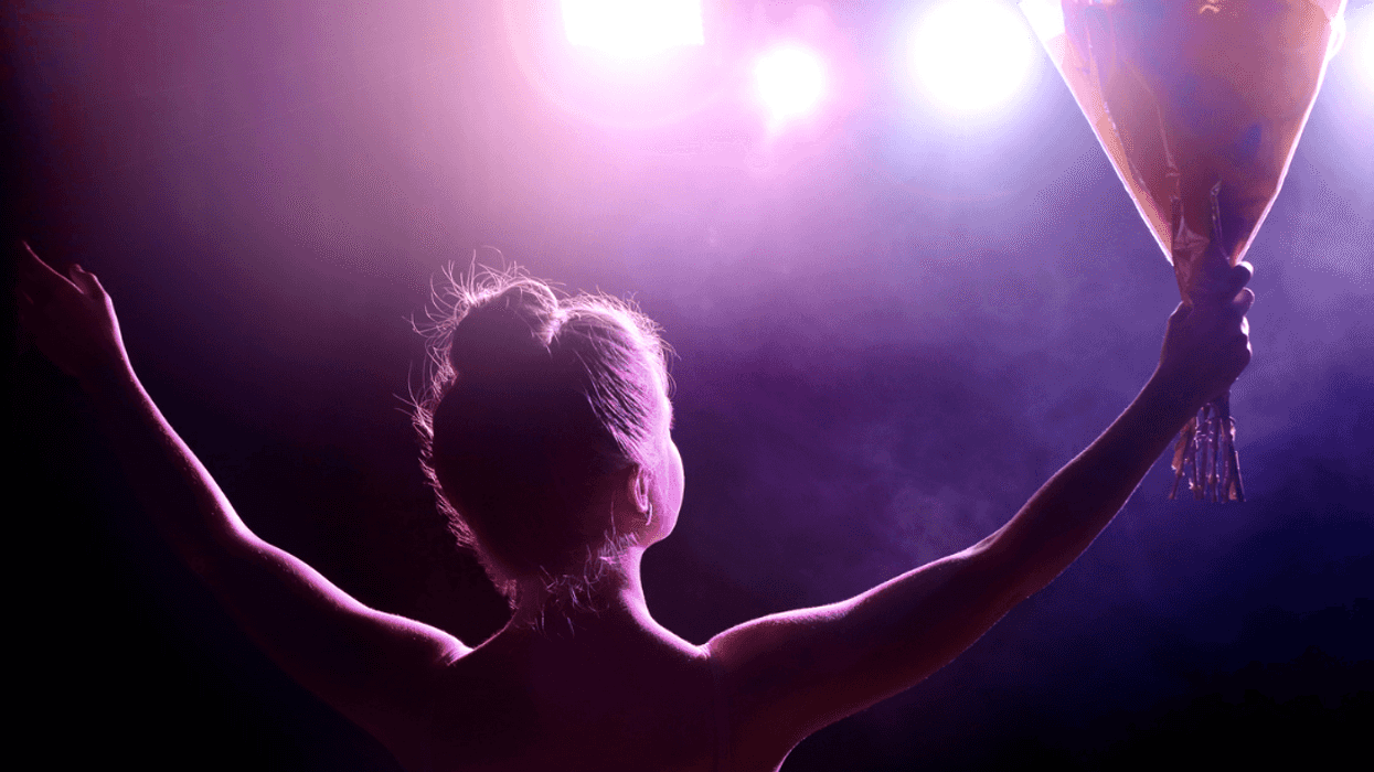 A woman on a stage holding out her arms and holding a bouquet of flowers.