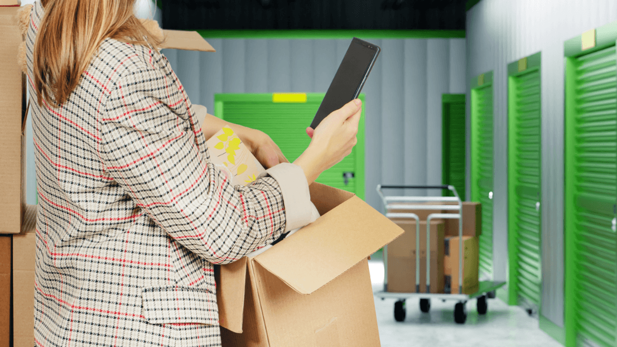 A woman on her phone holding a box in a storage facility.