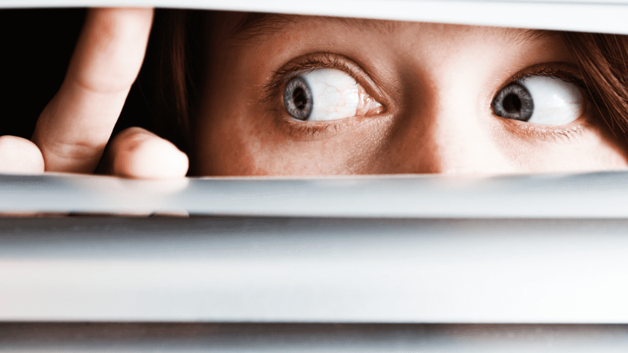 A woman peeking through blinds.