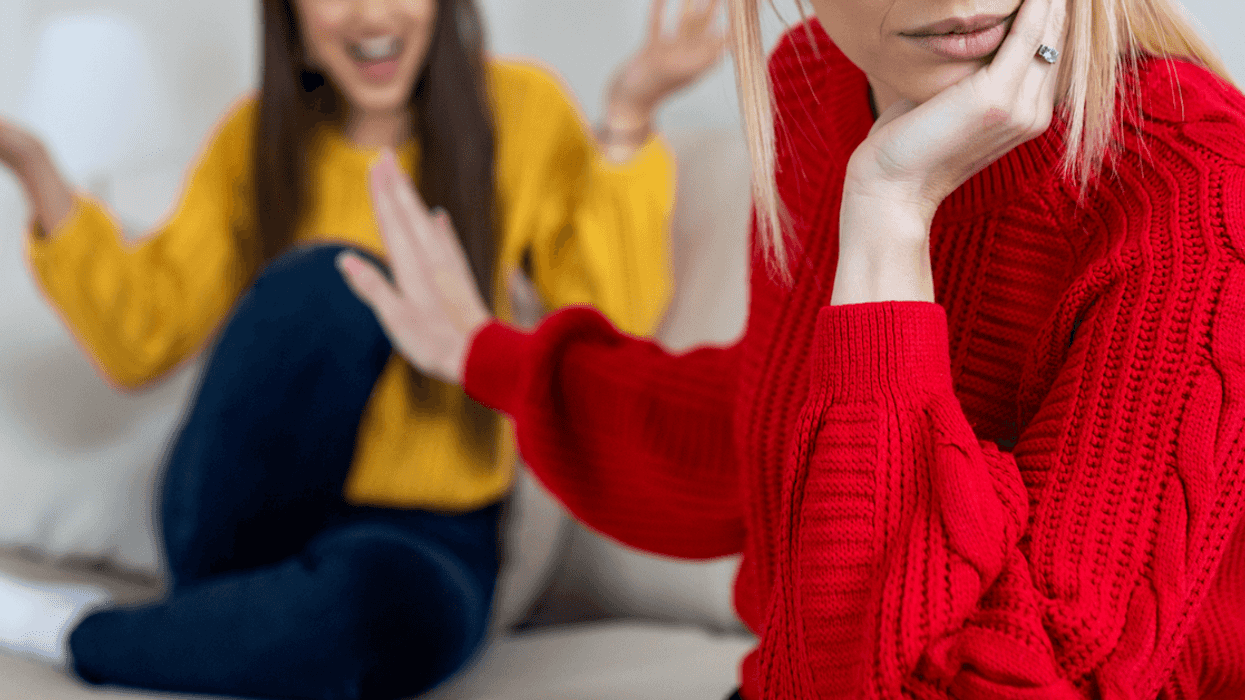 A woman pushing her hand in front of another woman sitting on the sofa.