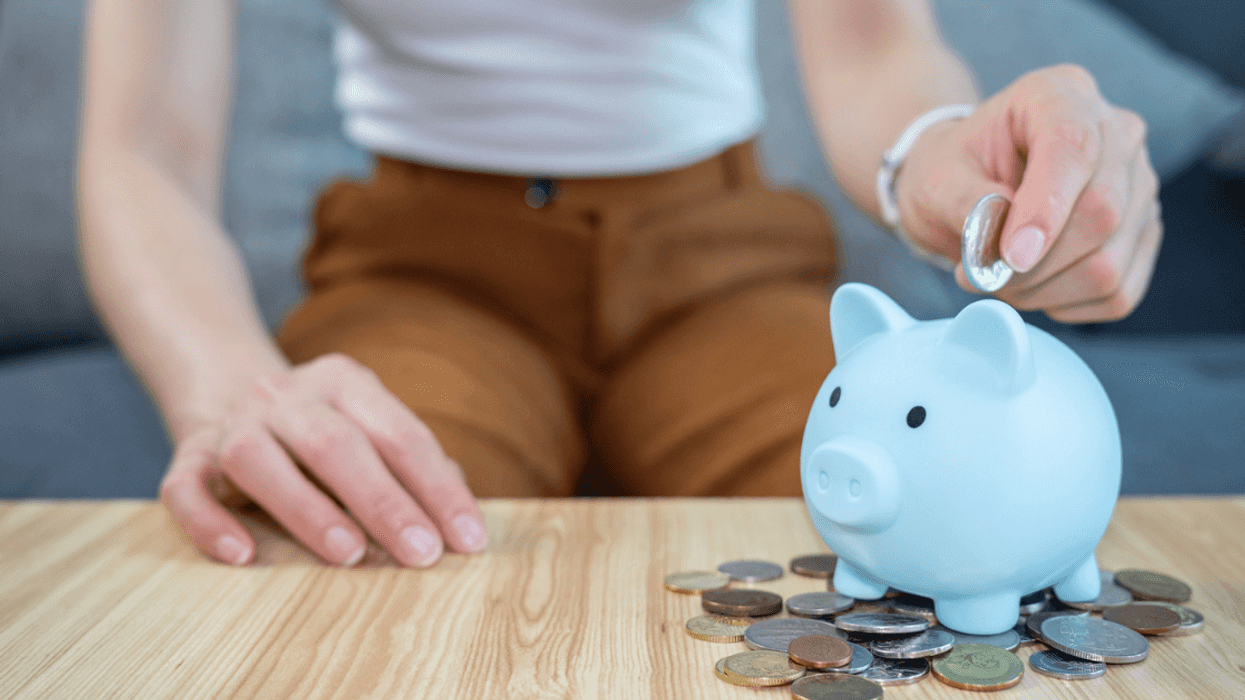 A woman putting a coin in a piggy bank.