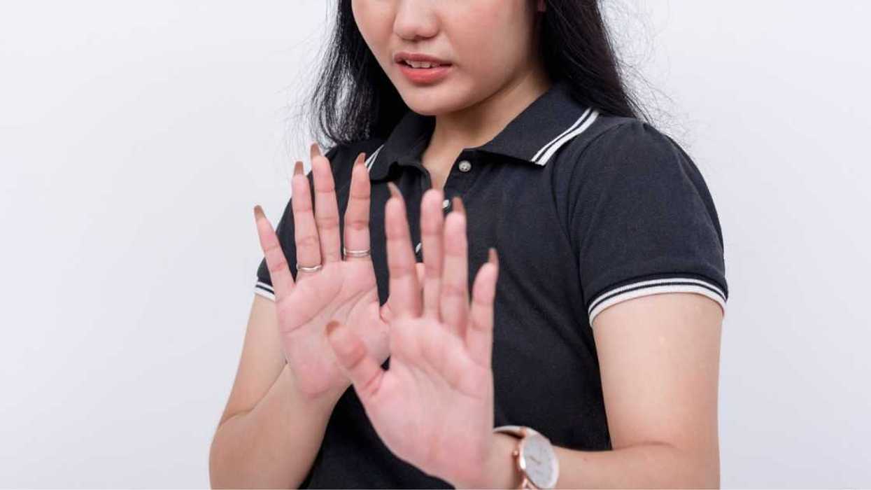 A woman refuses to come closer. Looking disgusted and appalled. Hands gesturing to stop. Isolated on a white background.