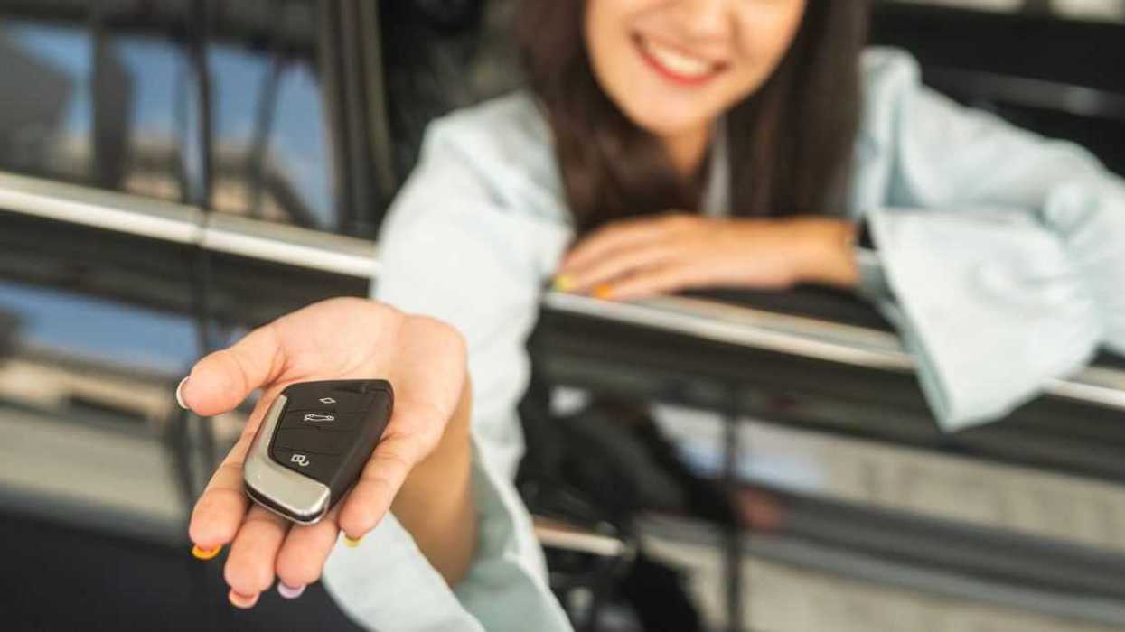 A woman's hand holds out a key to new car, through the open passenger side window.