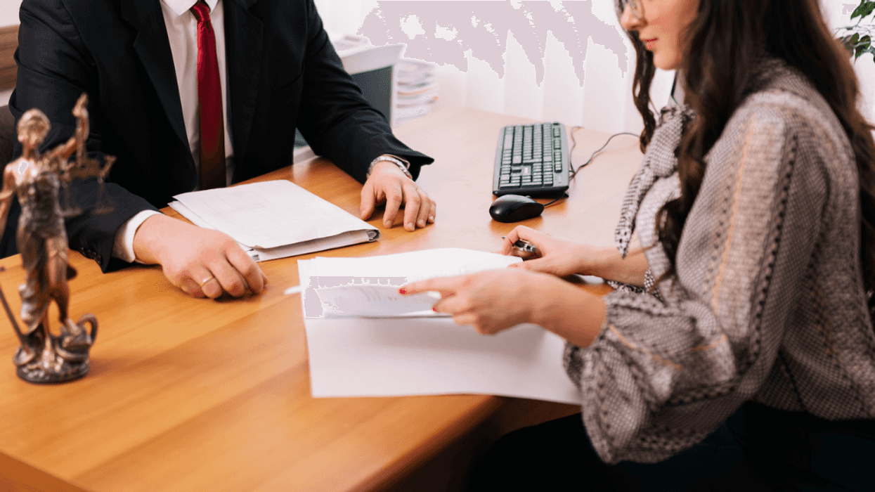 A woman seated opposite a suited man at a desk, looking over a document.