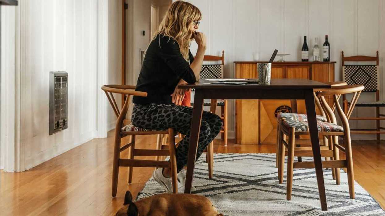 A woman sits alone at her dining table with her dog at her feet