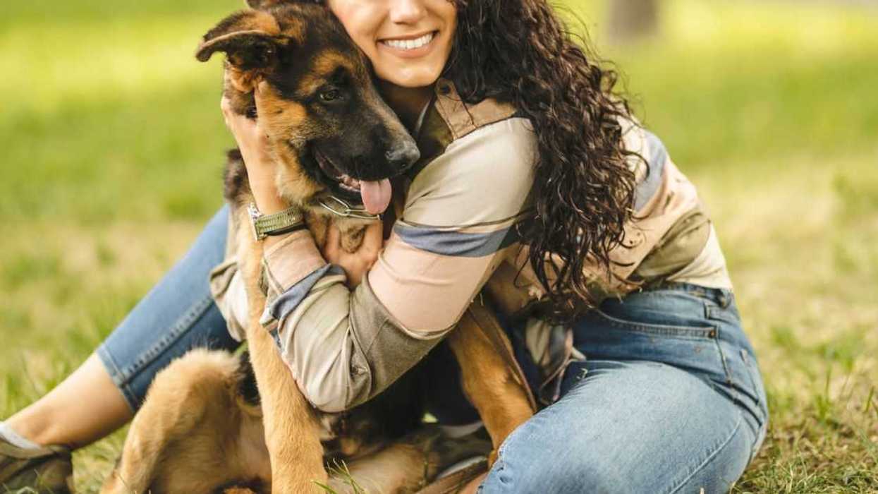 A woman sits in the park holding her german sheperd