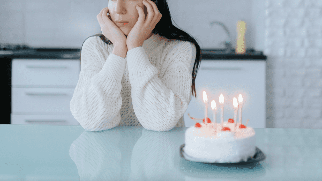 A woman sitting at a counter behind a birthday cake with candles in it.