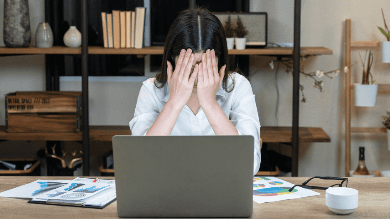 A woman sitting at a desk covering her face.