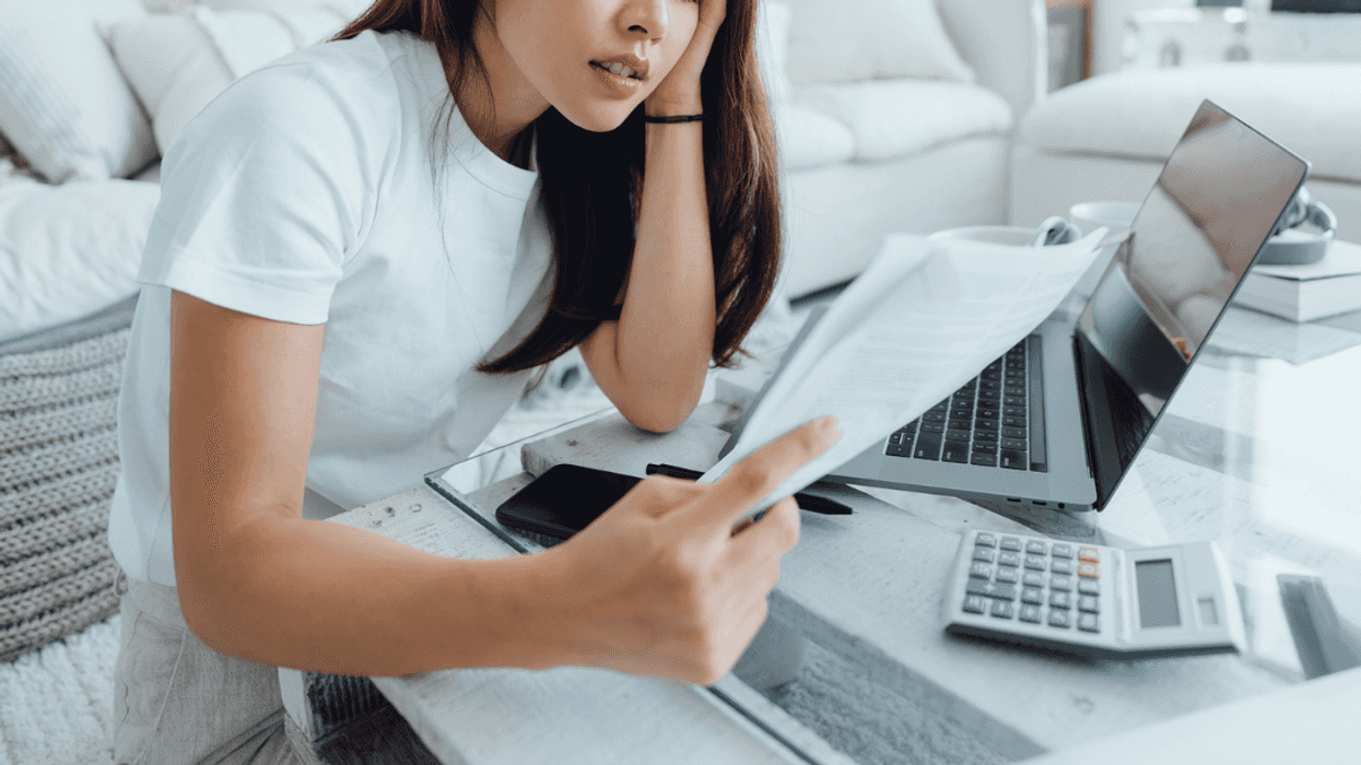 A woman sitting at a desk looking at a sheet of paper with a computer and a calculator nearby.