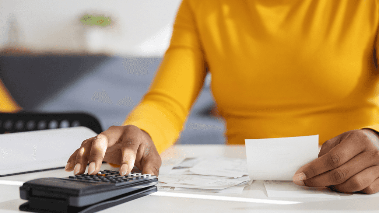 A woman sitting at a table with a calculator and paper receipts.