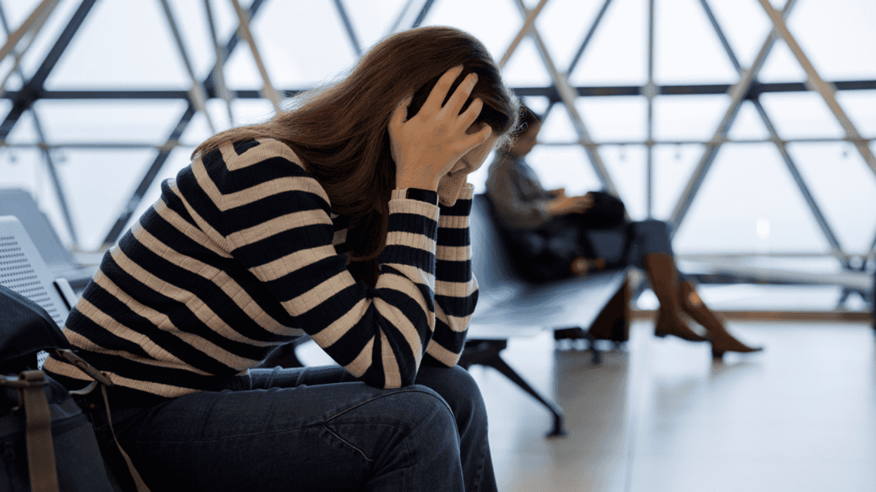 A woman sitting in an airport with her head in her hands.